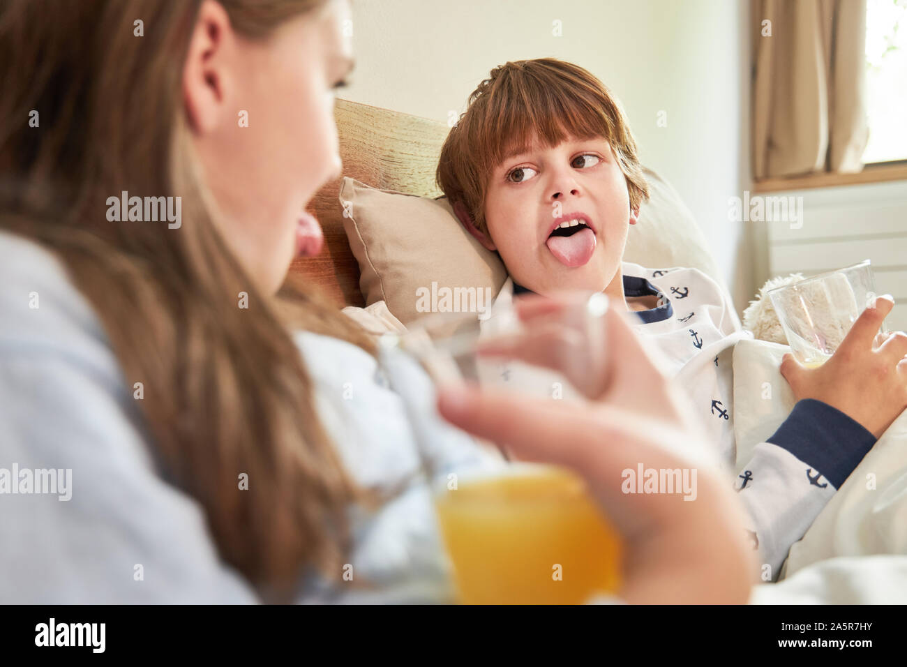 Naughty boy mostra la sua sorella la linguetta al mattino mentre si consuma la colazione a letto Foto Stock