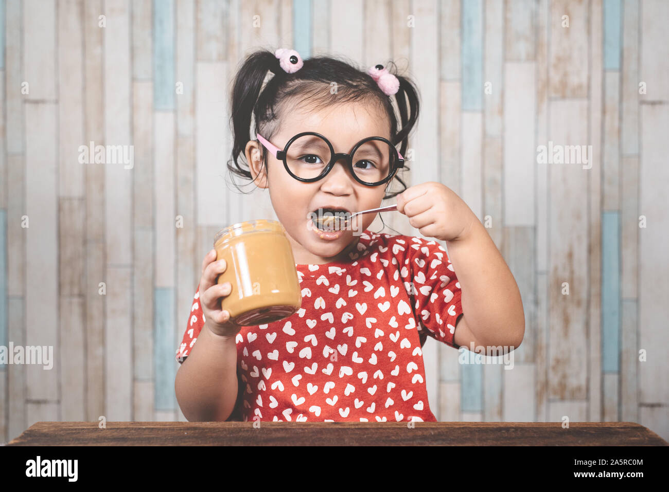 Poco ragazza asiatica holding e godendo di burro di arachidi in vaso e un cucchiaio, concetto di burro di arachidi amante Foto Stock