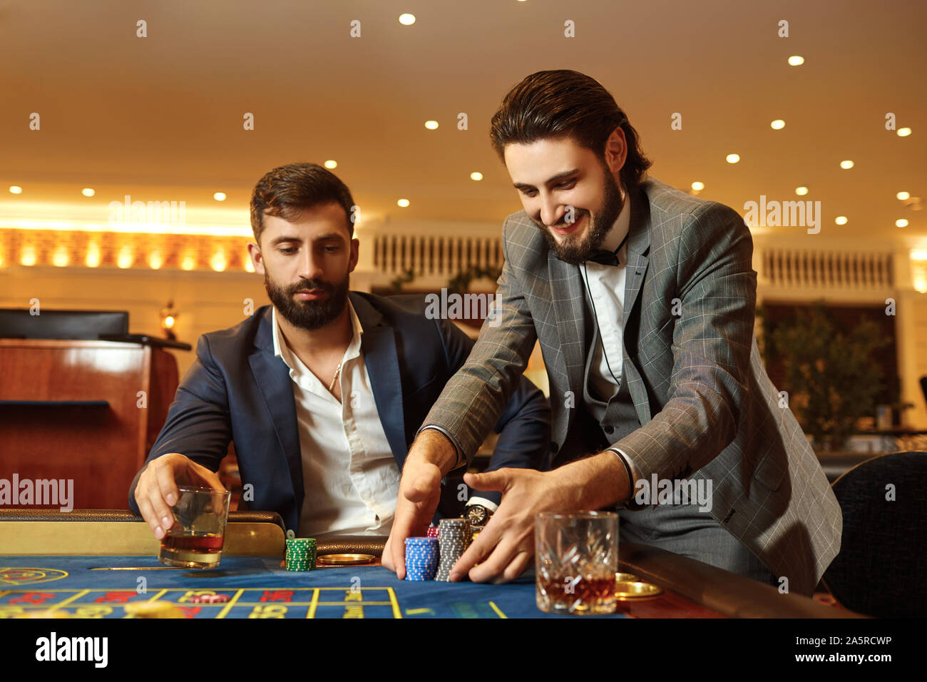 Uomo di gruppo in un vestito al tavolo della roulette giocando a poker in un casinò. Foto Stock