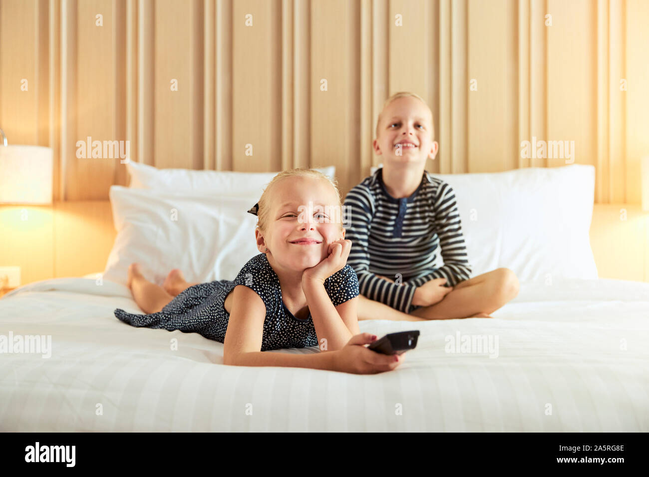 Sorridente bambina e suo fratello carino guardando la televisione togeter mentre vi rilassate in un letto Foto Stock