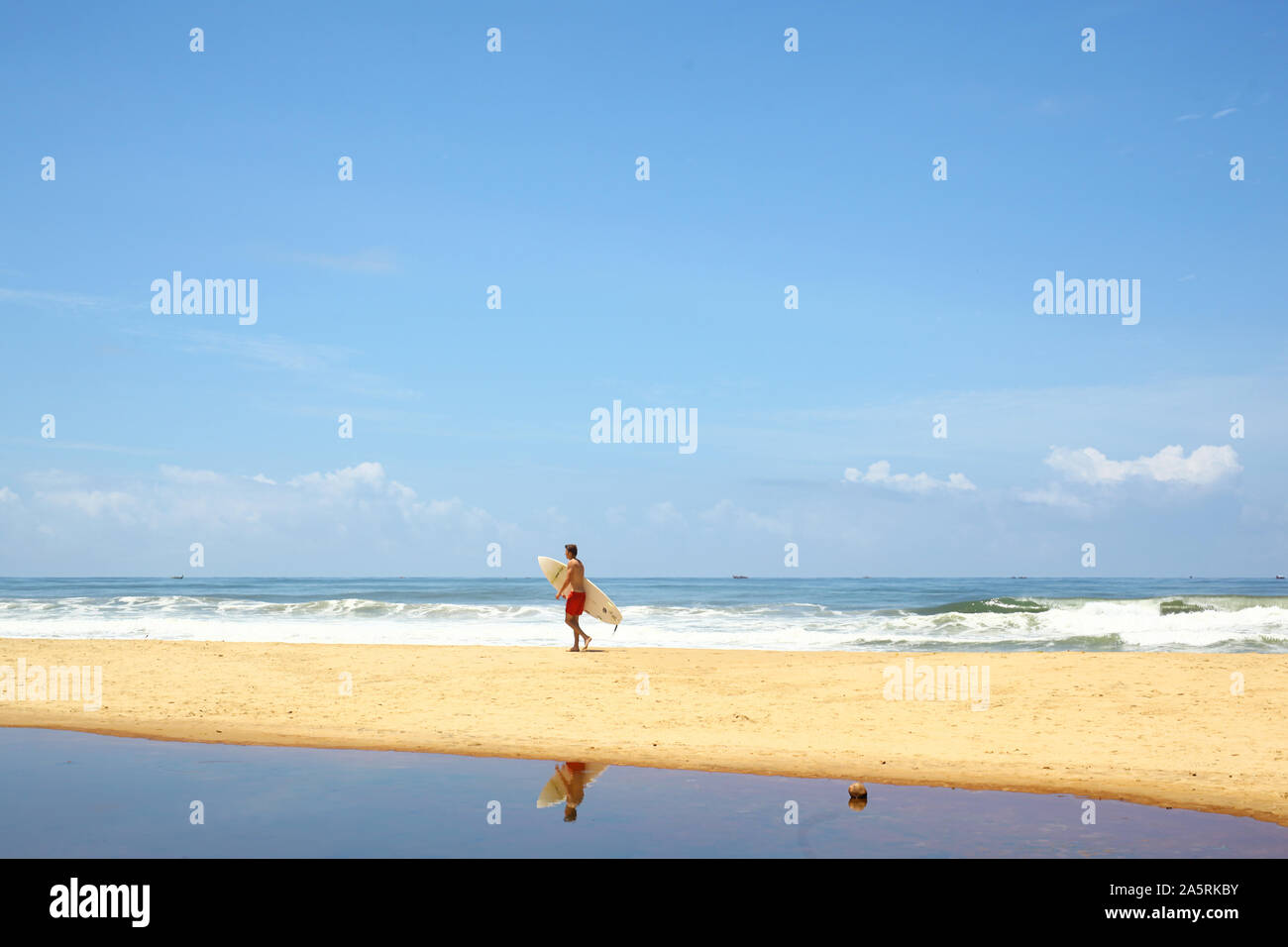 Un uomo a camminare sulla spiaggia con una tavola da surf Foto Stock