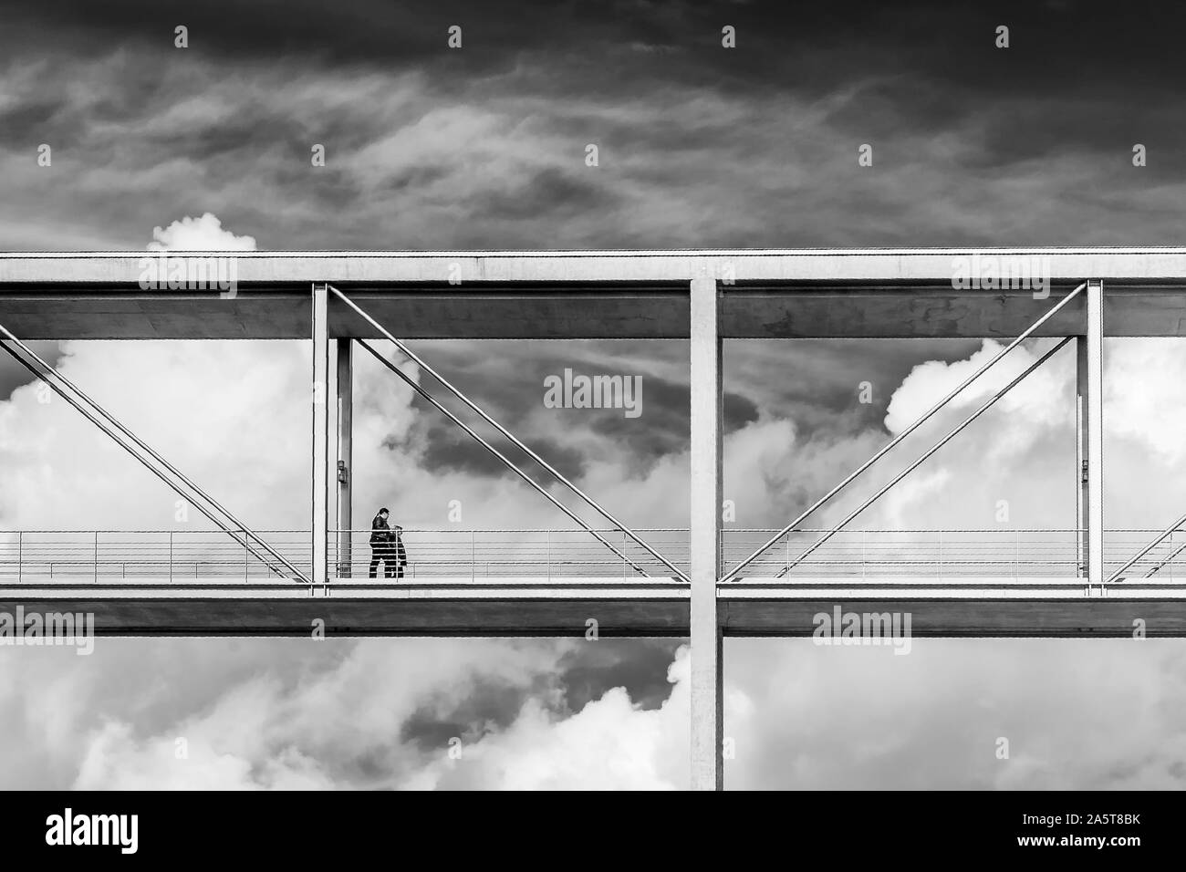 Bella in bianco e nero vista di due persone che camminano su un ponte di sospensione con una drammatica sky in background, distretto governativo di Berlino, Tedesco Foto Stock
