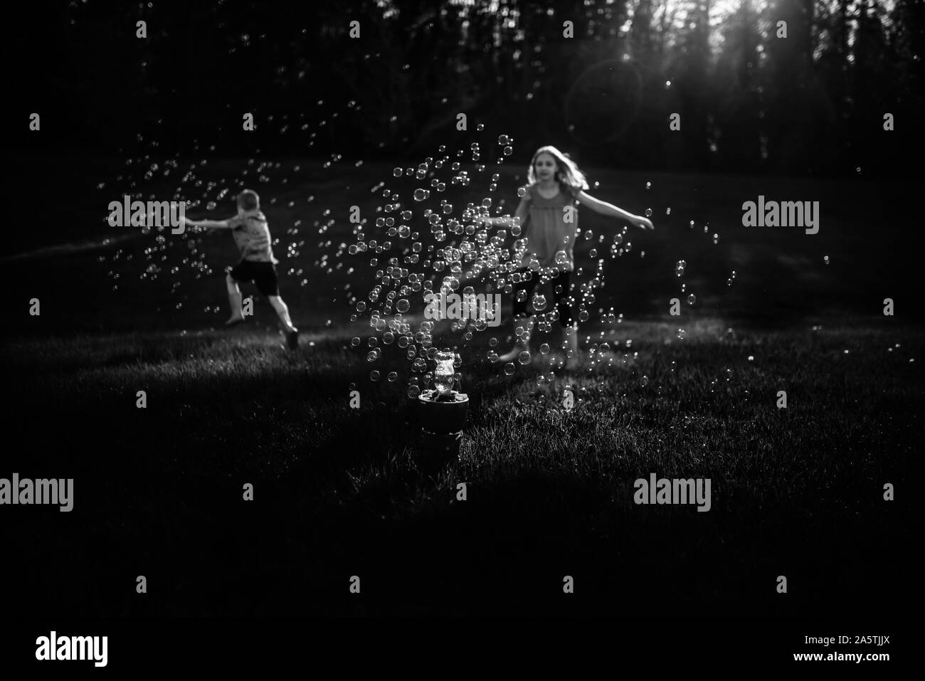 Immagine in bianco e nero dei fratelli che corre attraverso le bolle Foto Stock