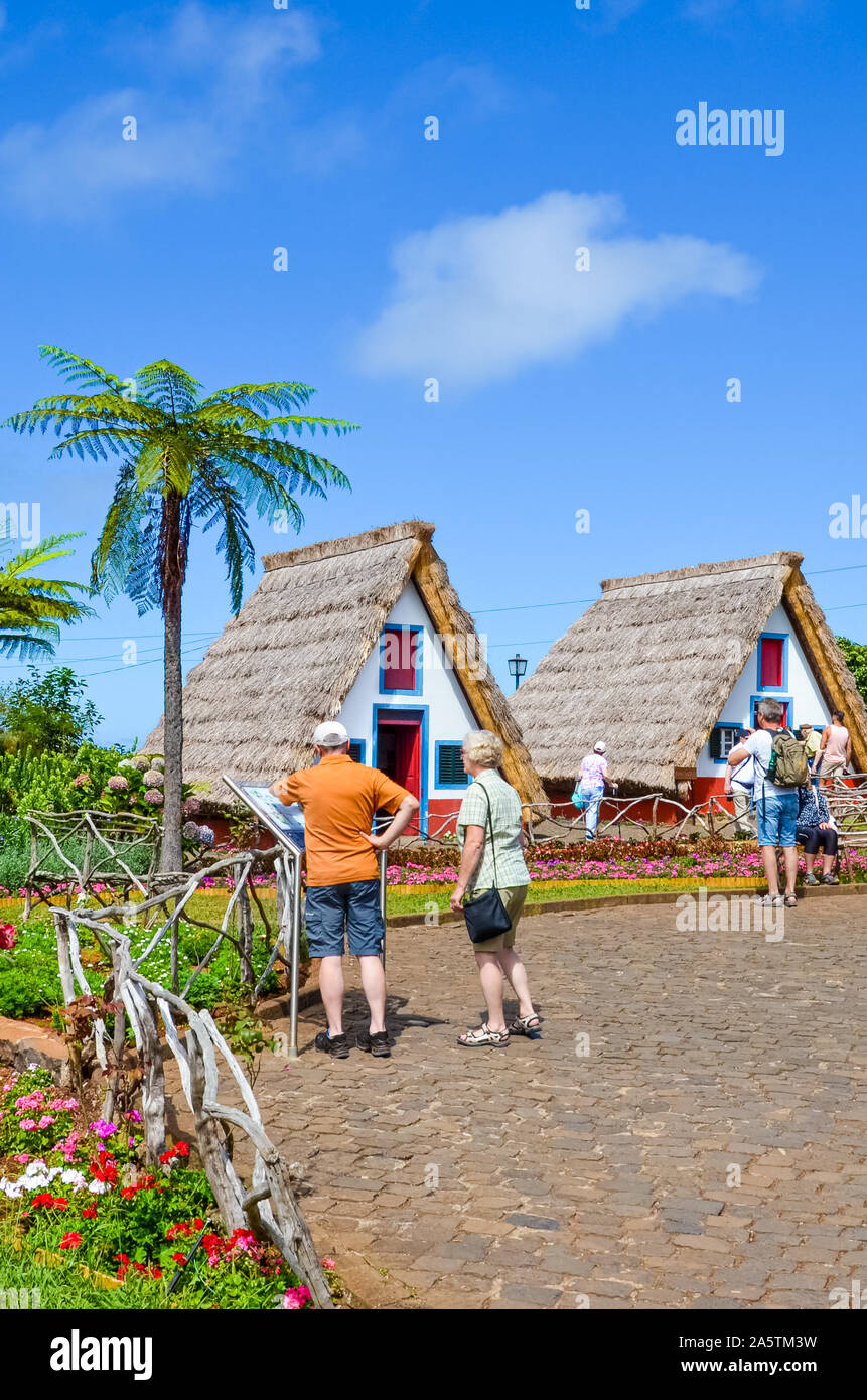 Santana, Madeira, Portogallo - Sep 24, 2019: Le tradizionali case colorate e turisti in giro. Una delle più popolari attrazioni turistiche dell'isola, patrimonio portoghese. Gli alberi di palma, giornata di sole. Foto Stock