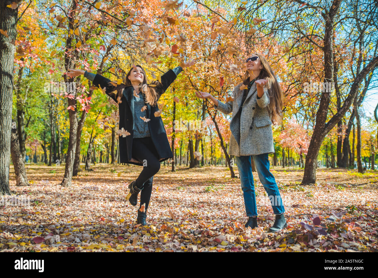 Due amiche ingannare intorno con foglie di giallo a City Park Foto Stock
