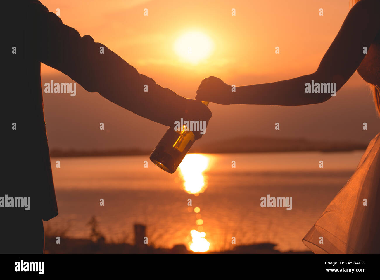 Un giovane è in possesso di una bottiglia di vino nelle loro mani con i sunsetin sullo sfondo. Che cosa un momento romantico. Foto Stock