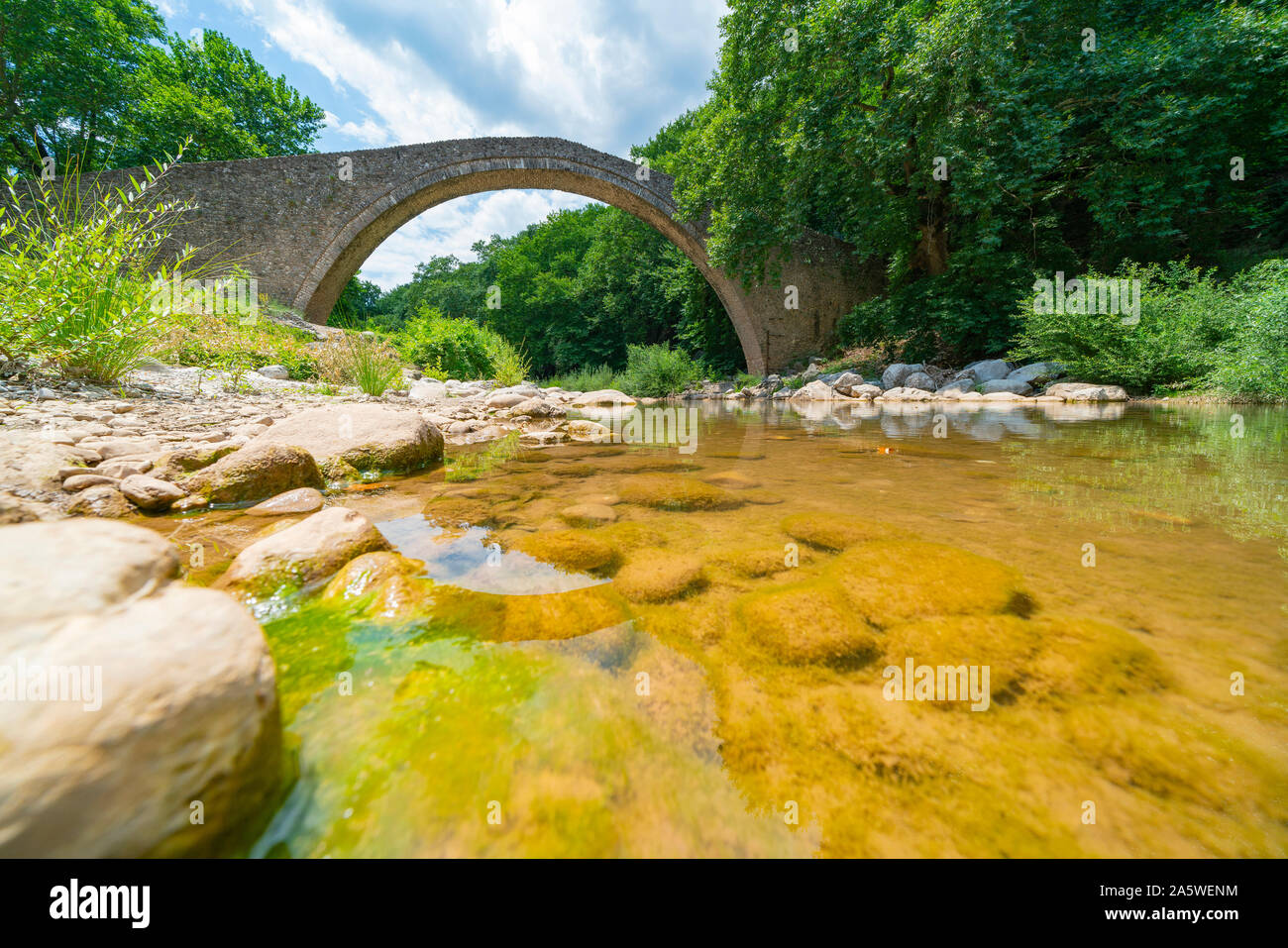 Stony river con alge coperto pietre subacqueo che scorre sotto la pietra storica unica arcata pedestrial ponte a Zagori in montagne in Grecia centrale. Foto Stock