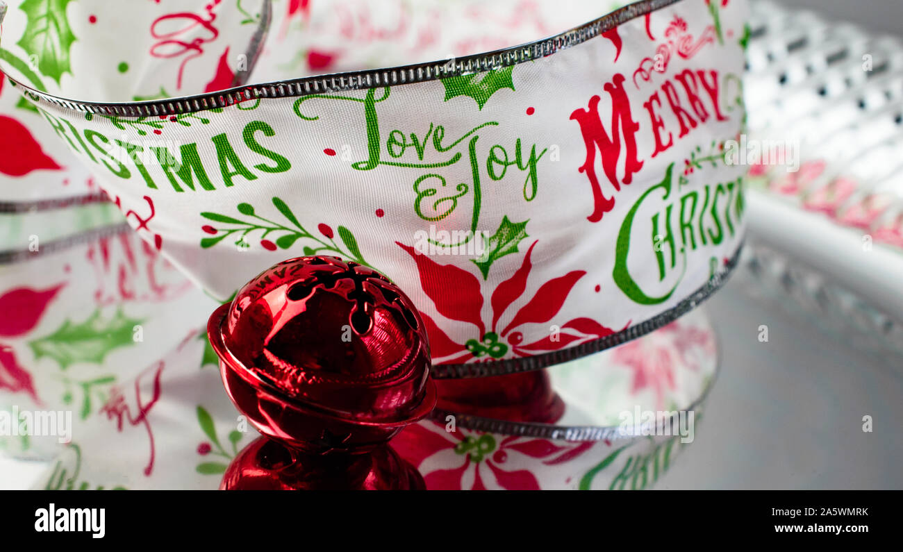 Red Jingle Bell e di elementi decorativi Buon Natale nastro con le parole di amore e gioia in rosso e verde su argento superficie riflettente Foto Stock