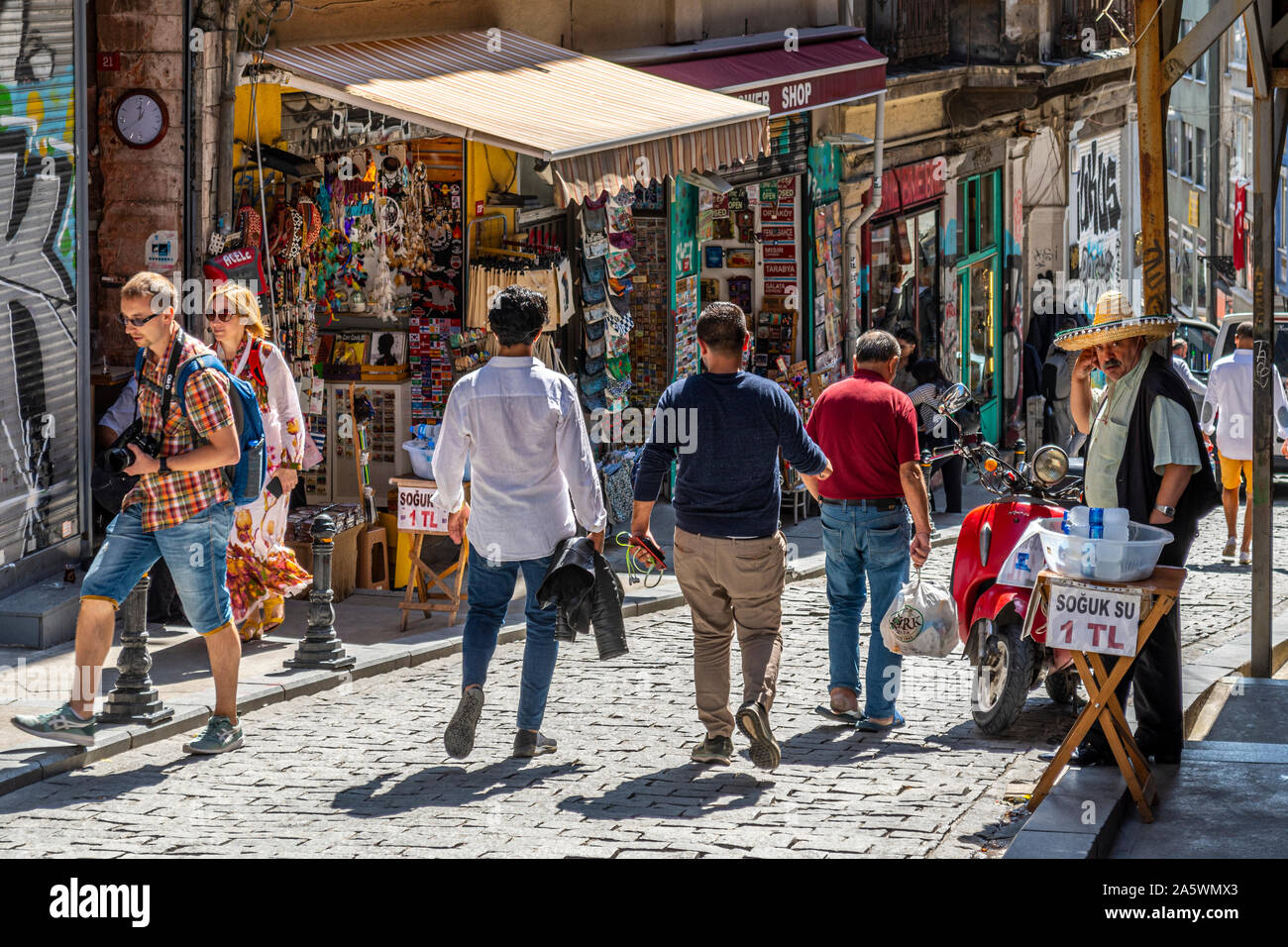 Un Turk vende acqua imbottigliata sul marciapiede vicino a negozi di souvenir e colorati negozi di articoli da regalo in zona collinare in quartiere di Galata di Istanbul in Turchia Foto Stock