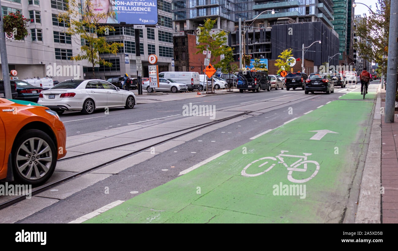 Pista ciclabile verde su una strada trafficata nel centro di Toronto come ciclista è visto in lontananza. Foto Stock