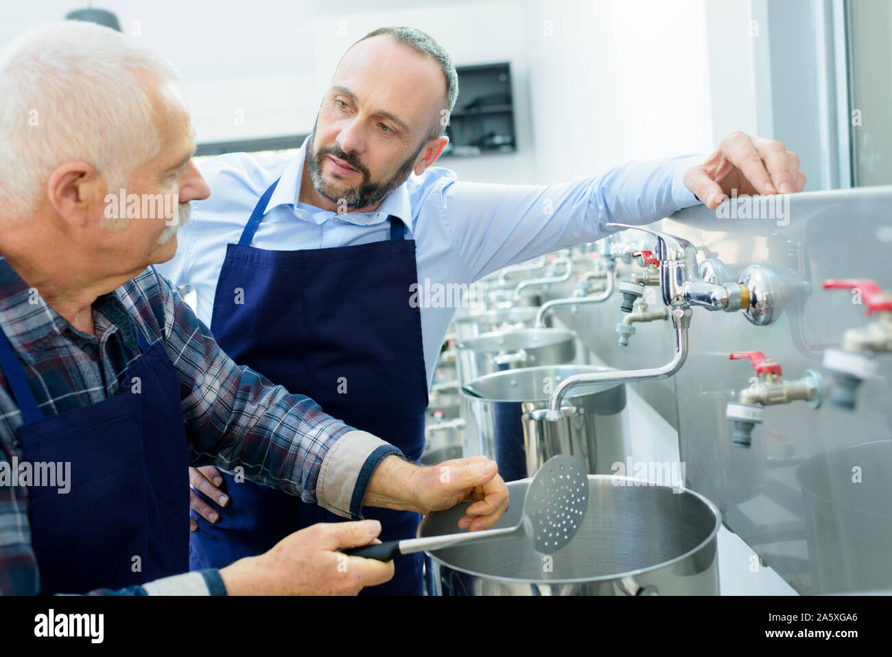 Lavoratore con mestolo forato dalla fila di acciaio inox padelle Foto Stock