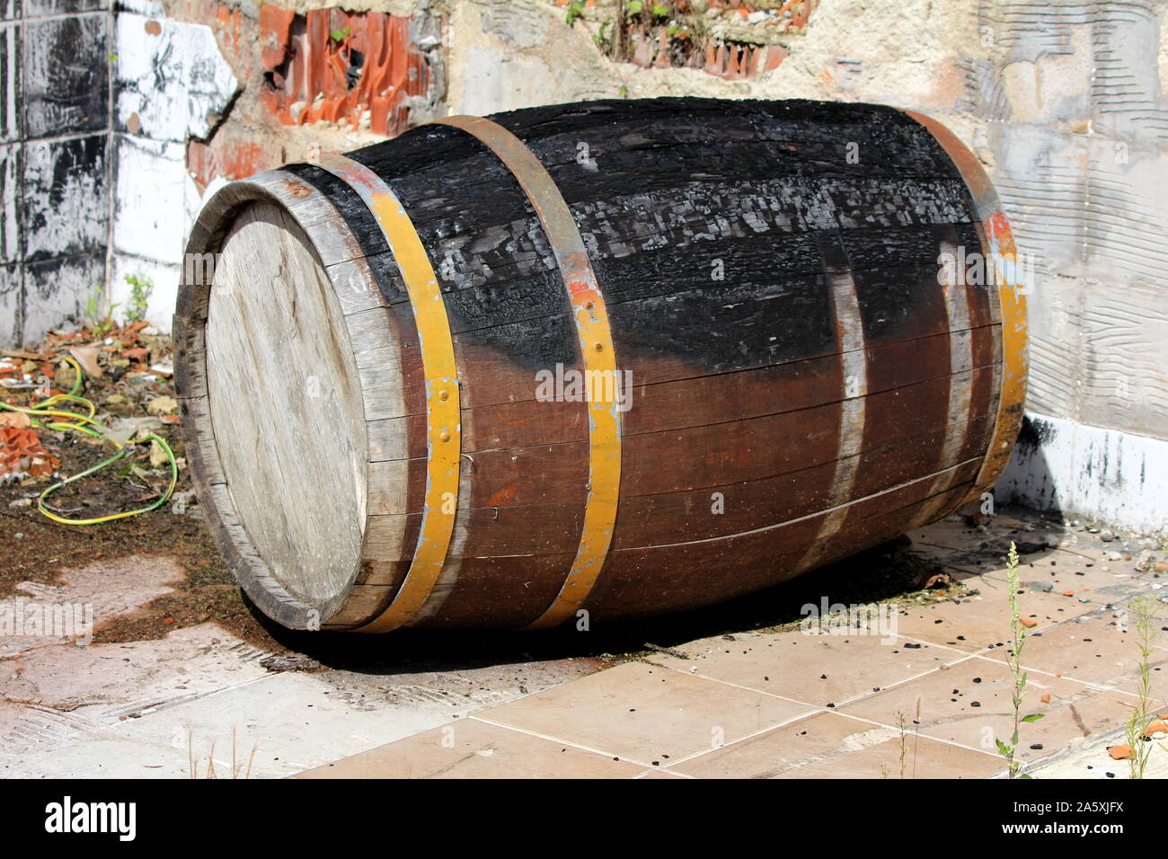 Vecchio vintage in legno, grande botte di vino bruciato su un lato durante la casa famiglia fire sinistro esterno circondato con piastrelle rotte e di materiale di costruzione Foto Stock