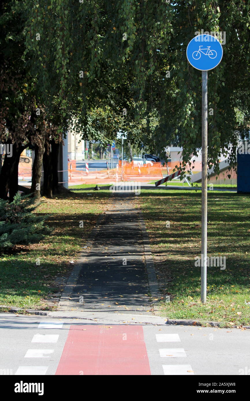 Round blu e bianco inizio della pista ciclabile lane road segno accanto alla bicicletta lastricata via circondato da erba coperto con foglie cadute e alberi Foto Stock