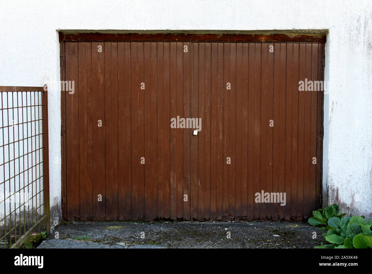 Metallo arrugginito vecchio rustico vintage porte di garage con recinzione metallica su un lato e calcestruzzo vialetto davanti a caldo e soleggiato giorno di estate Foto Stock