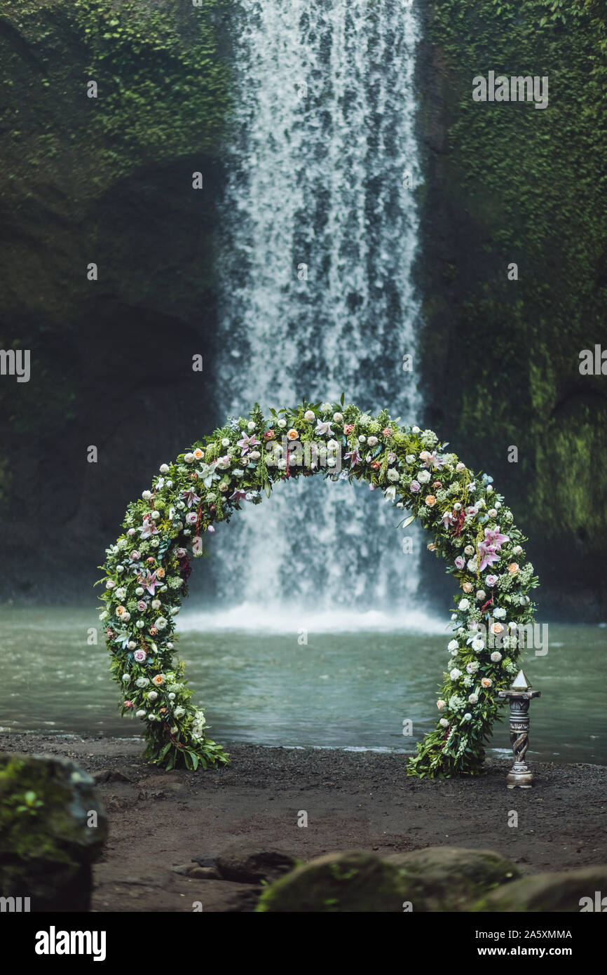 Cerimonia di nozze su Tibumana cascata, Bali. Arco rotondo con fiori freschi nella giungla. Natura insolita concetto di matrimonio. Foto Stock
