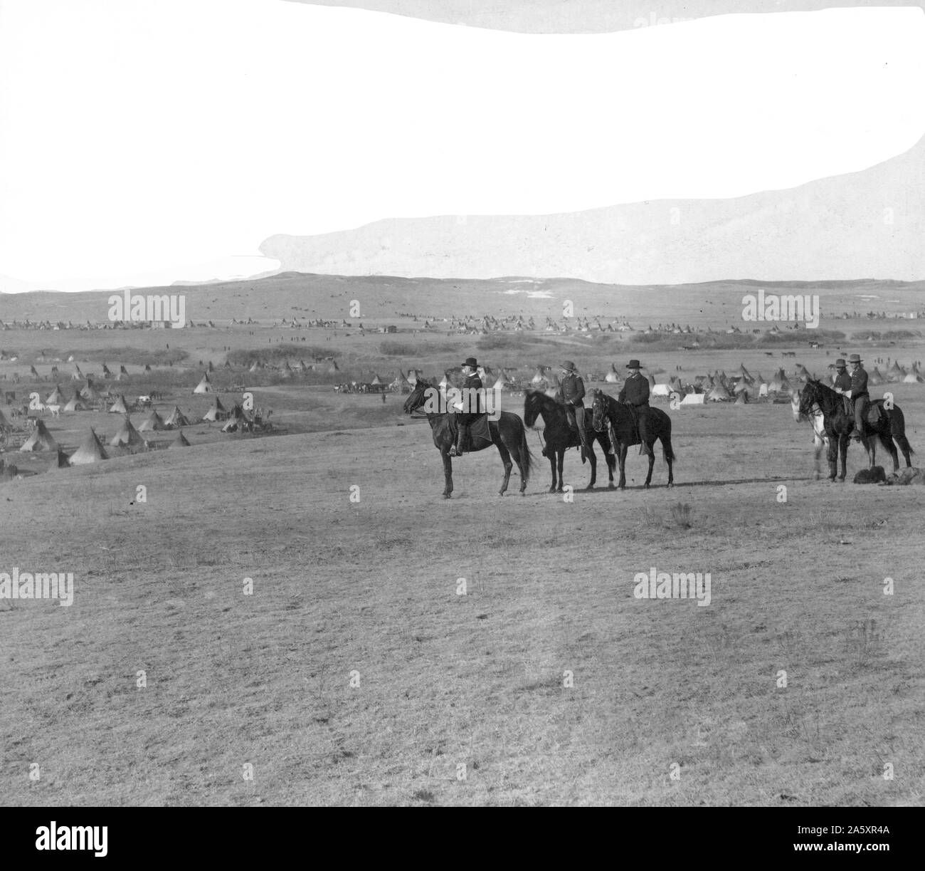 Sei uomini militare a cavallo su una collina che si affaccia su un grande accampamento di tipis. Foto Stock