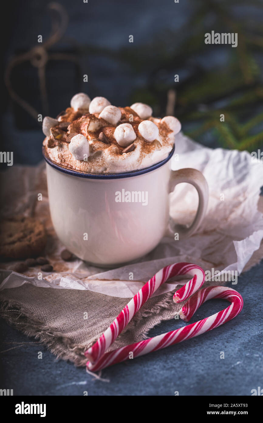 Lussuoso cioccolata calda con panna montata e pezzi di marshmallows e scaglie di cioccolato in una tazza di colore bianco su sfondo blu. Di fronte all'chocol Foto Stock