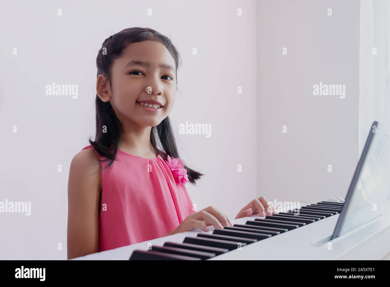 Una piccola ragazza asiatica suonare la tastiera bianca con la felicità. I  bambini indossare un abito rosa pratica il pianoforte con divertimento e  sorridente Foto stock - Alamy