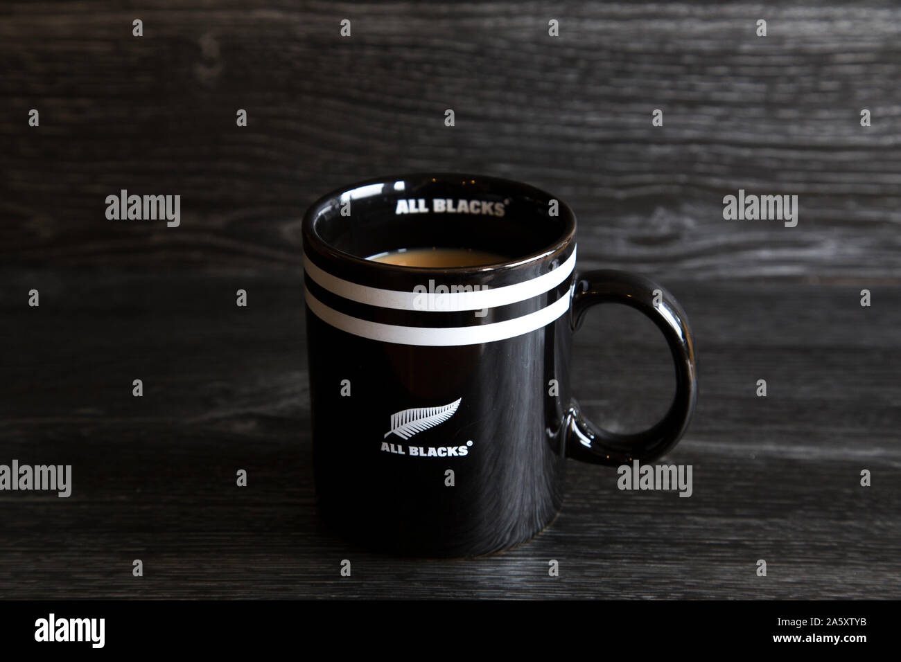 Tazza di tè ricavato in un All Blacks cup. Tutti i neri sono una delle migliori squadre di rugby in tutto il mondo. Forte tè bianco seduto su di un legno scuro banco di cucina. Foto Stock