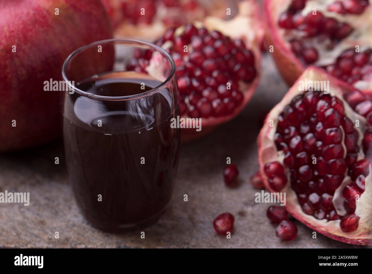 Un bicchiere di organico sano succo di melograno , accanto a fette di melograno. La frutta e i succhi di frutta sono su un rustico in pietra superficie. Vista orizzontale sli Foto Stock