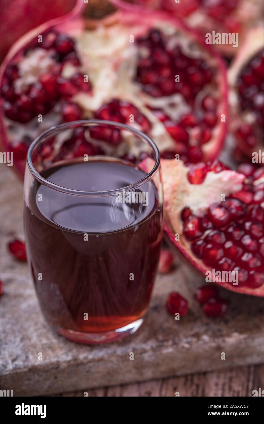 Un bicchiere di organico sano succo di melograno , accanto a fette di melograno. La frutta e i succhi di frutta sono su un rustico in pietra superficie. Vista verticale leggero Foto Stock