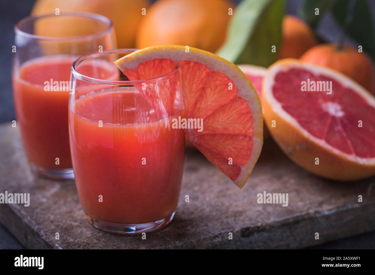 Sano sangue organica di succo d'arancia con sangue pompelmi e pomeli e le arance al buio su un superficie di pietra. Sfondo scuro, con frutta sfocati foglie. Foto Stock