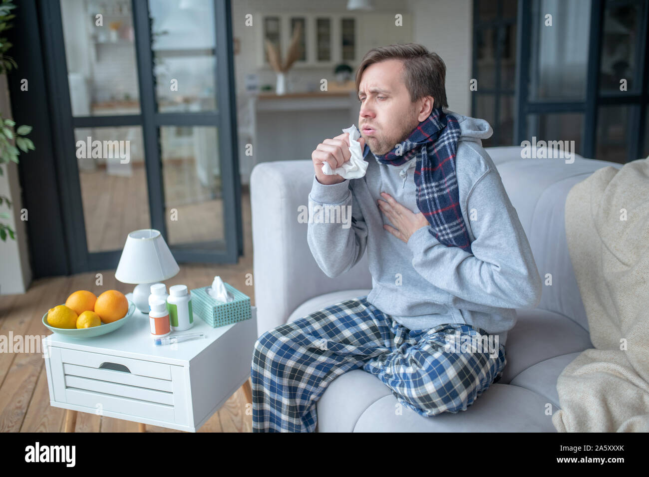 Uomo seduto sul divano e tosse dopo assunzione di vitamine Foto Stock