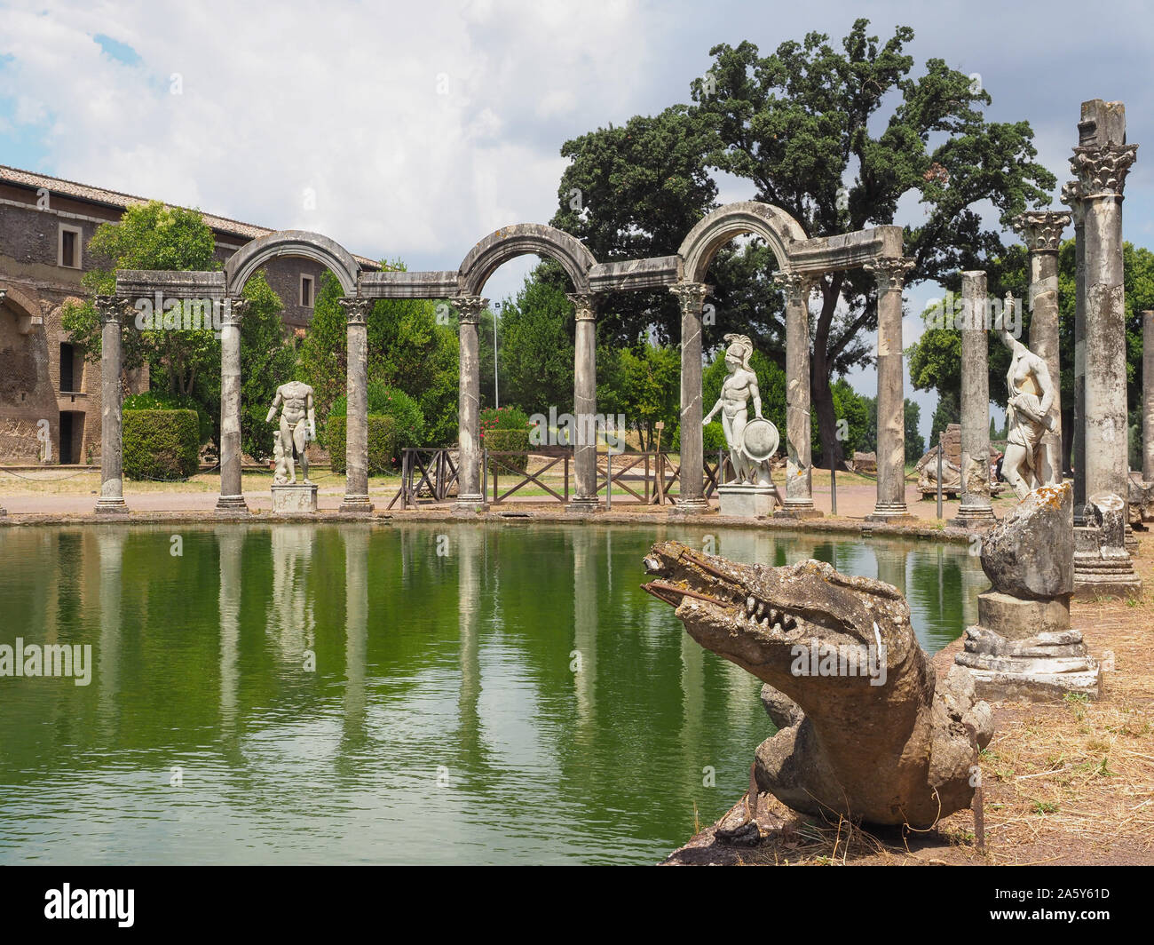 Colonne in rovina, sculture in marmo e coccodrillo sul lato curvo di canal-piscina Canopo. Parco architettonico, Villa Adriana, creato dell imperatore Adriano Foto Stock