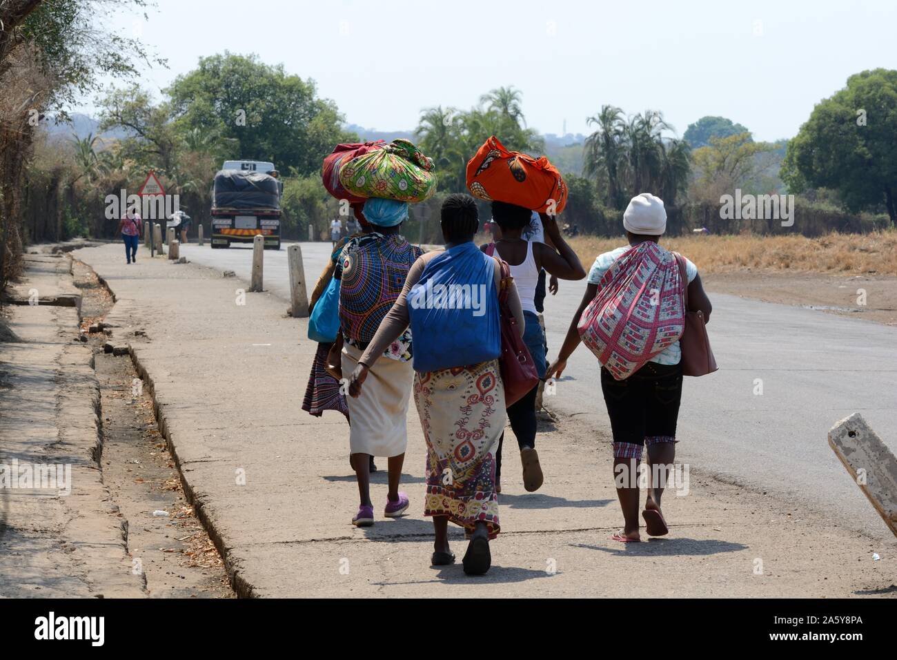 Donne persone che trasportano carichi pesanti che indossano vestiti tradizionali sulla frontiera tra Zambia e Zimbabwe Africa Foto Stock