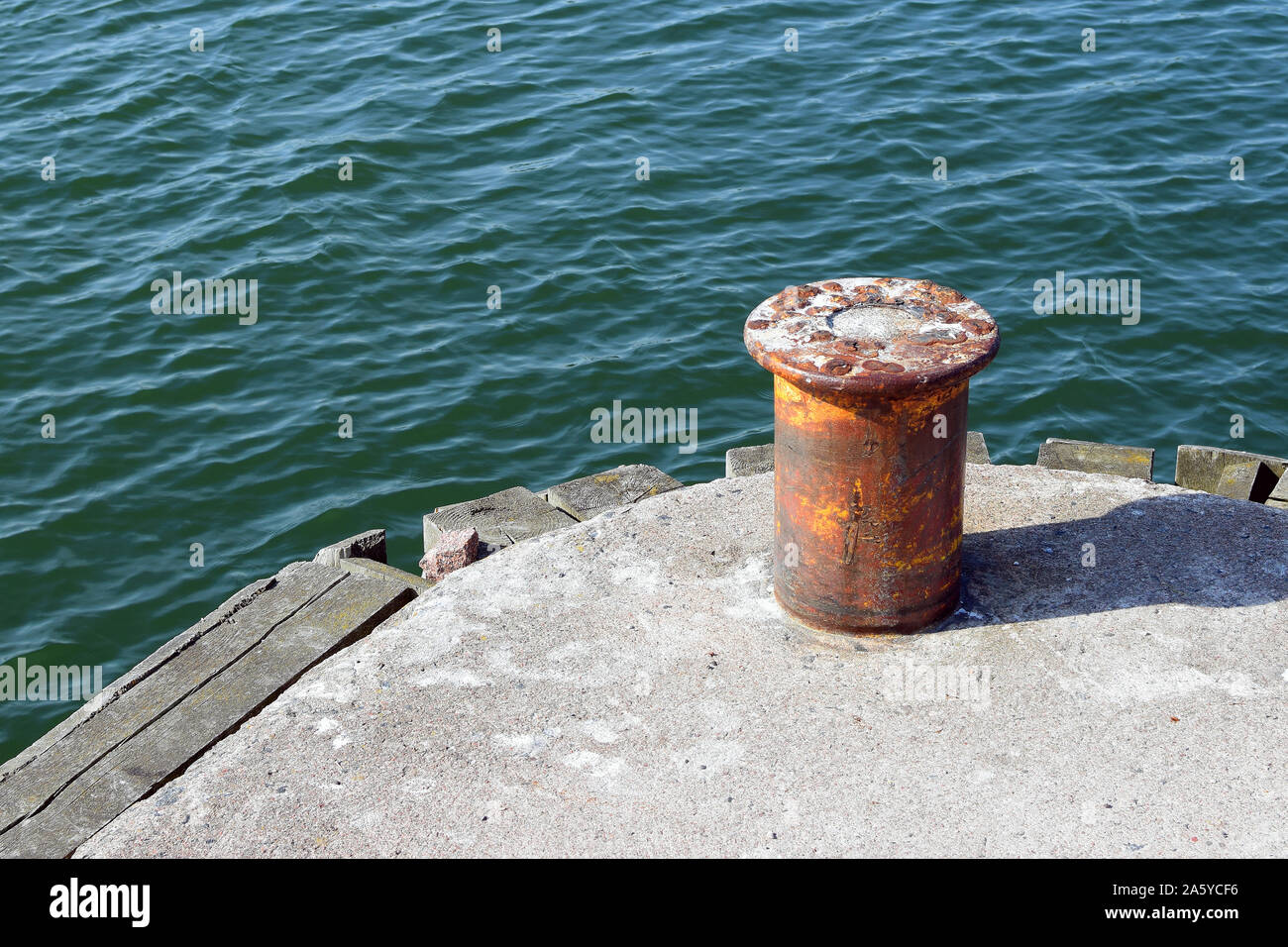 Vecchio arrugginito bollard ormeggio sul molo del porto e di acqua con piccole onde. Copia dello spazio. Foto Stock