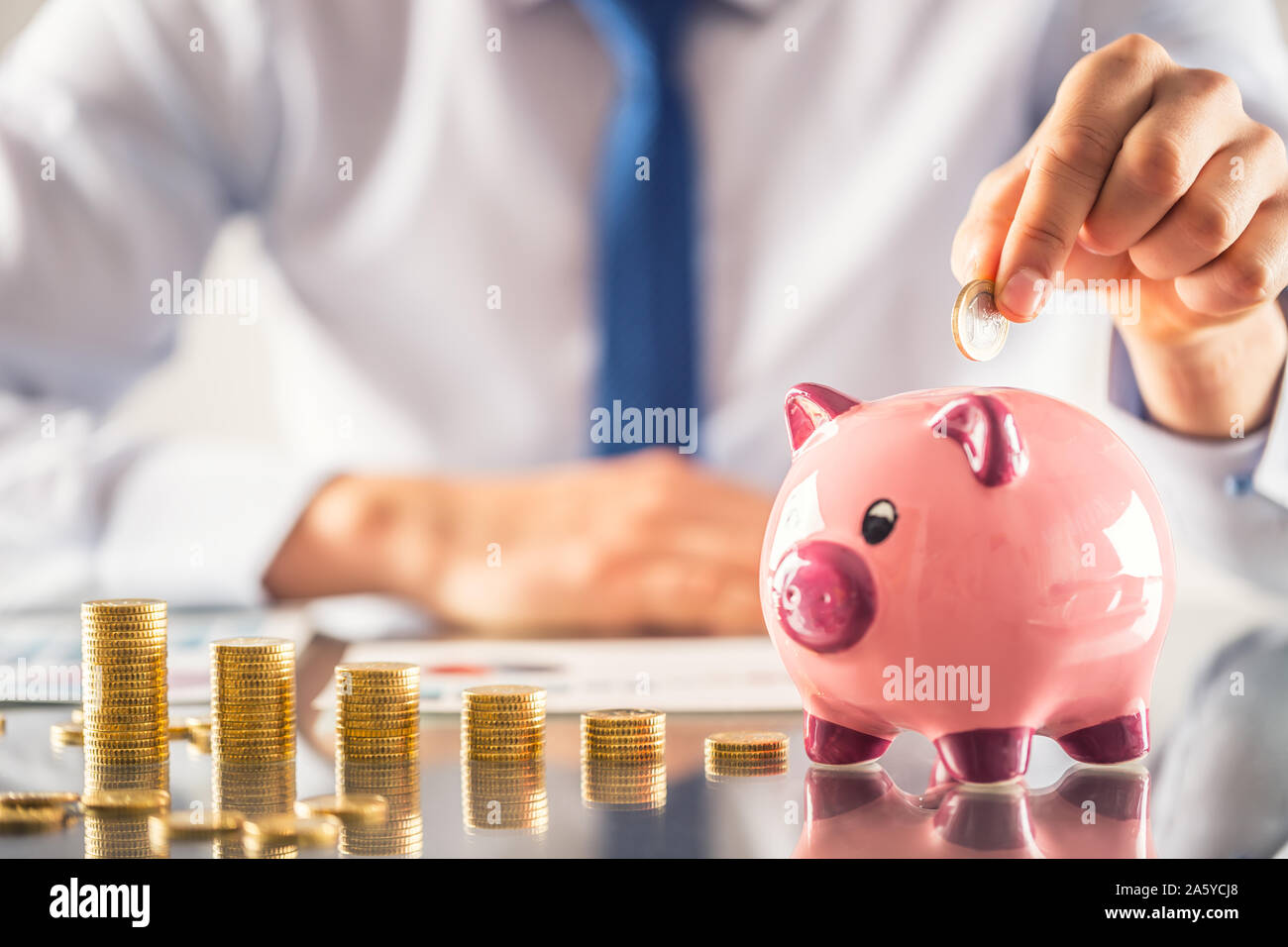 Banchiere commercialista o assicuratore mettere soldi in un salvadanaio. Tabella finanziaria da monete concetto aziendale Foto Stock