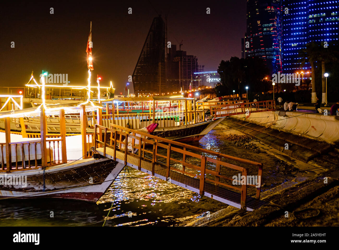 In legno barche Dhow, equipaggiato con strisce di luce, sedersi in attesa per il noleggio in tarda serata su Doha Corniche Foto Stock