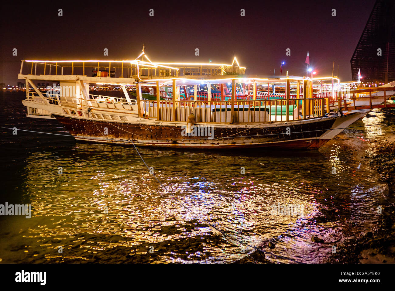 In legno barche Dhow, equipaggiato con strisce di luce, sedersi in attesa per il noleggio in tarda serata su Doha Corniche Foto Stock