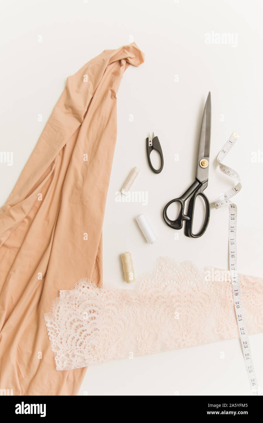 Il lavoro di una sarta. Forbici, tessuto, una cucitura Ripper, il centimetro e filettatura su uno sfondo bianco. Appartamento laico, vista dall'alto, copyspace. Foto Stock