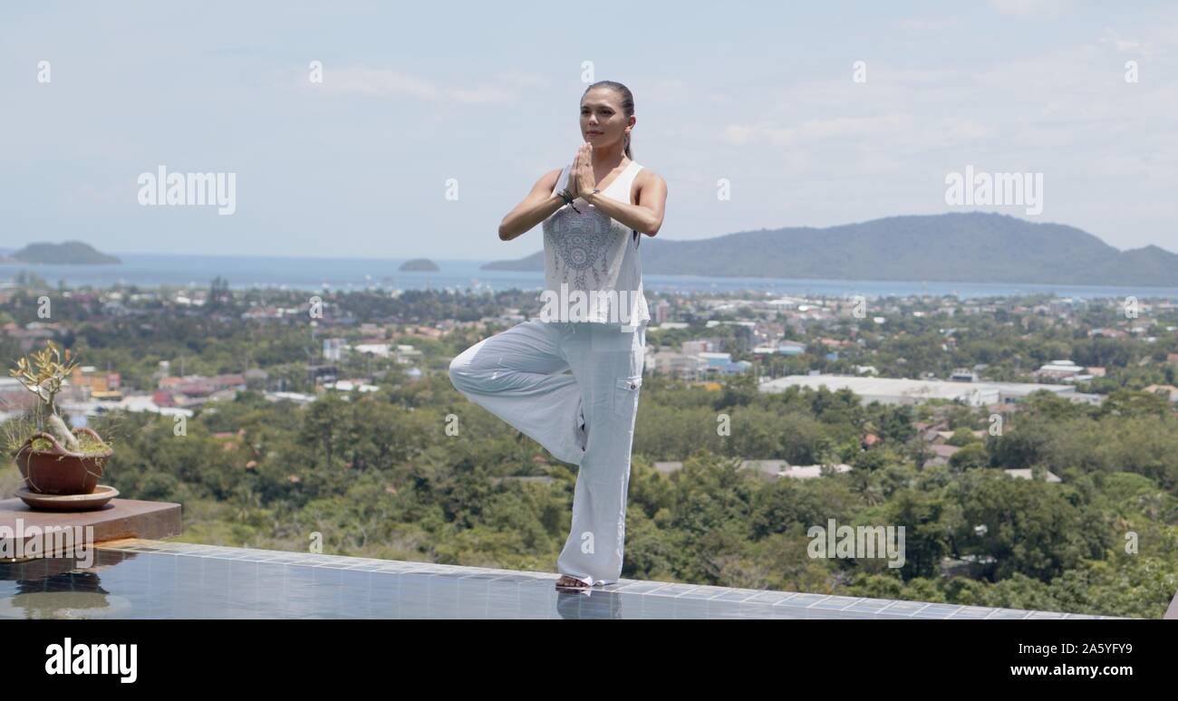 Donna adulta a praticare yoga in piscina contro un paesaggio fantastico Foto Stock