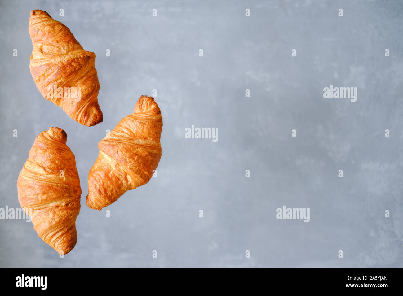 Tre i croissant appena sfornati volare su sfondo grigio. Posto per il testo. Creative concetto da forno Foto Stock