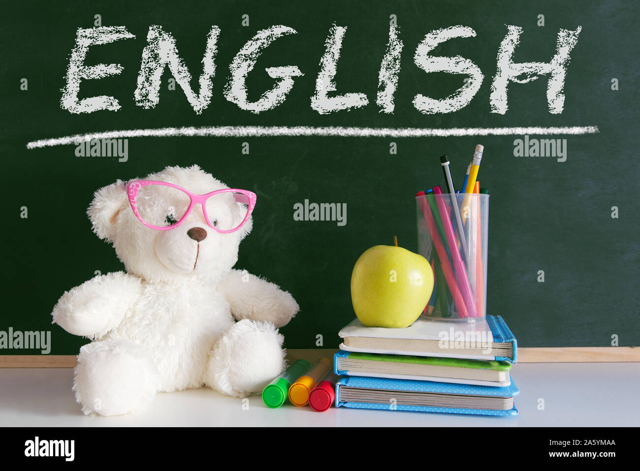 La parola 'English' scritti su una lavagna in una classe di lingua per i primi bambini educazione. Accanto, un orsacchiotto di peluche che indossa gli occhiali, matite colorate e alcuni Foto Stock