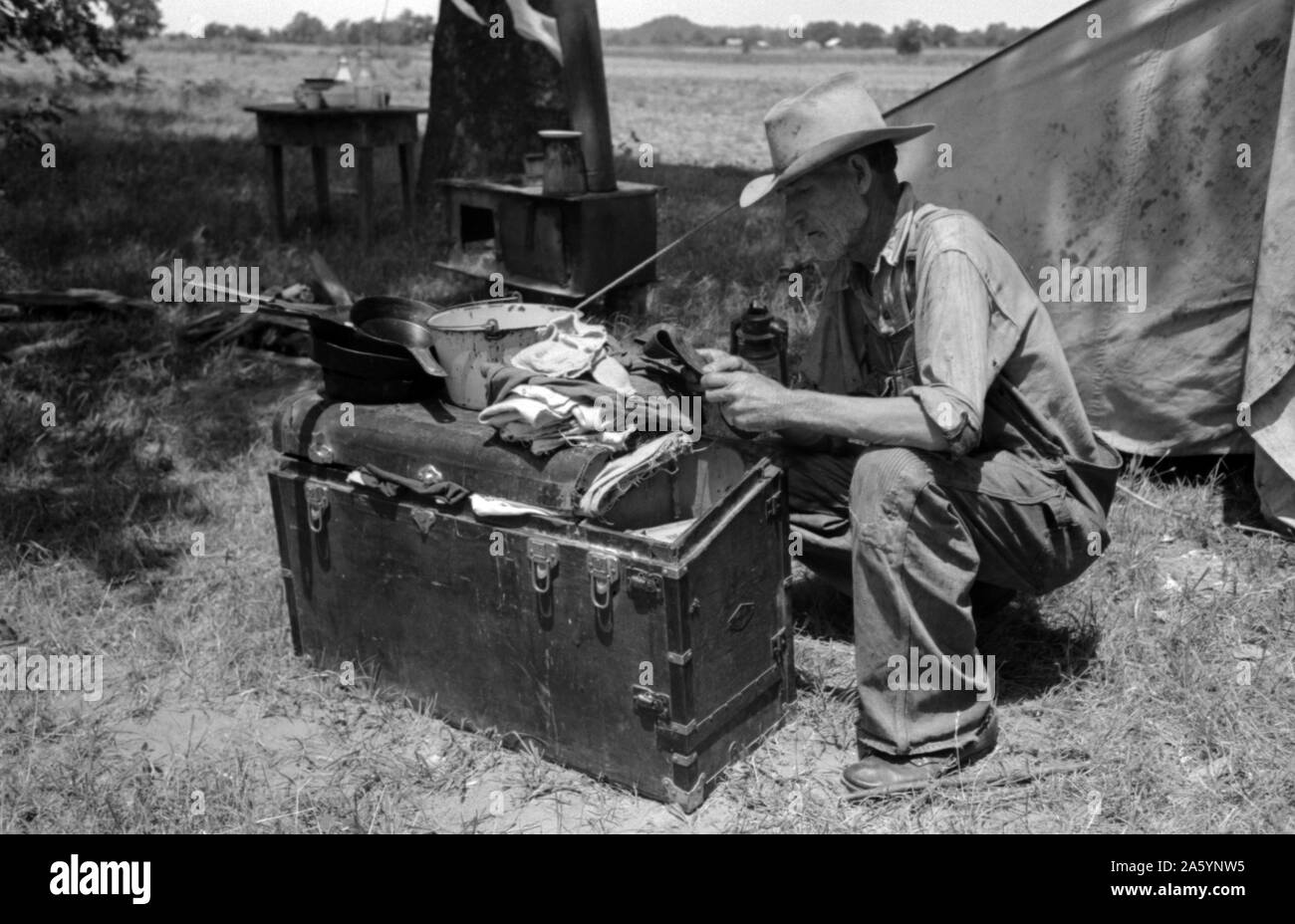 Veterano migrante lavoratore agricolo esaminando il contenuto del suo tronco si accampò sul fiume Arkansas in Wagoner County, Oklahoma, 19390101. Da Russell Lee, 1903-1986, fotografo Foto Stock