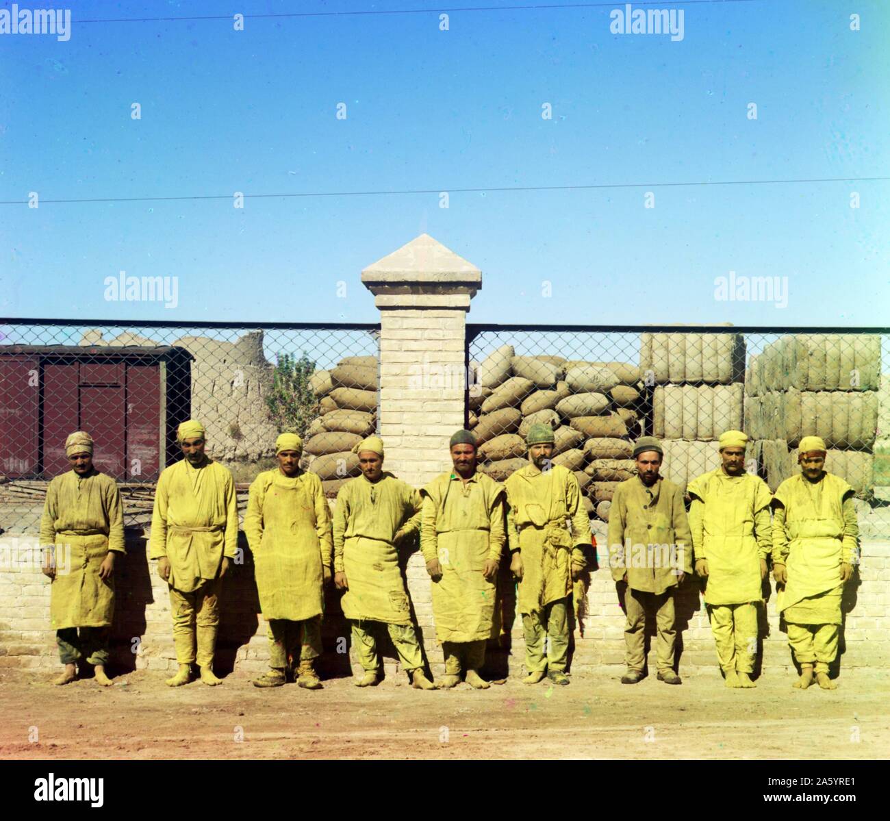 Un gruppo di operai in piedi, in bilico, di fronte a una catena di collegamento recinto, con sacchi accatastati dietro il recinto. Prokudin-Gorskii, Sergei Mikhailovich, 1863-1944, fotografo. Foto Stock