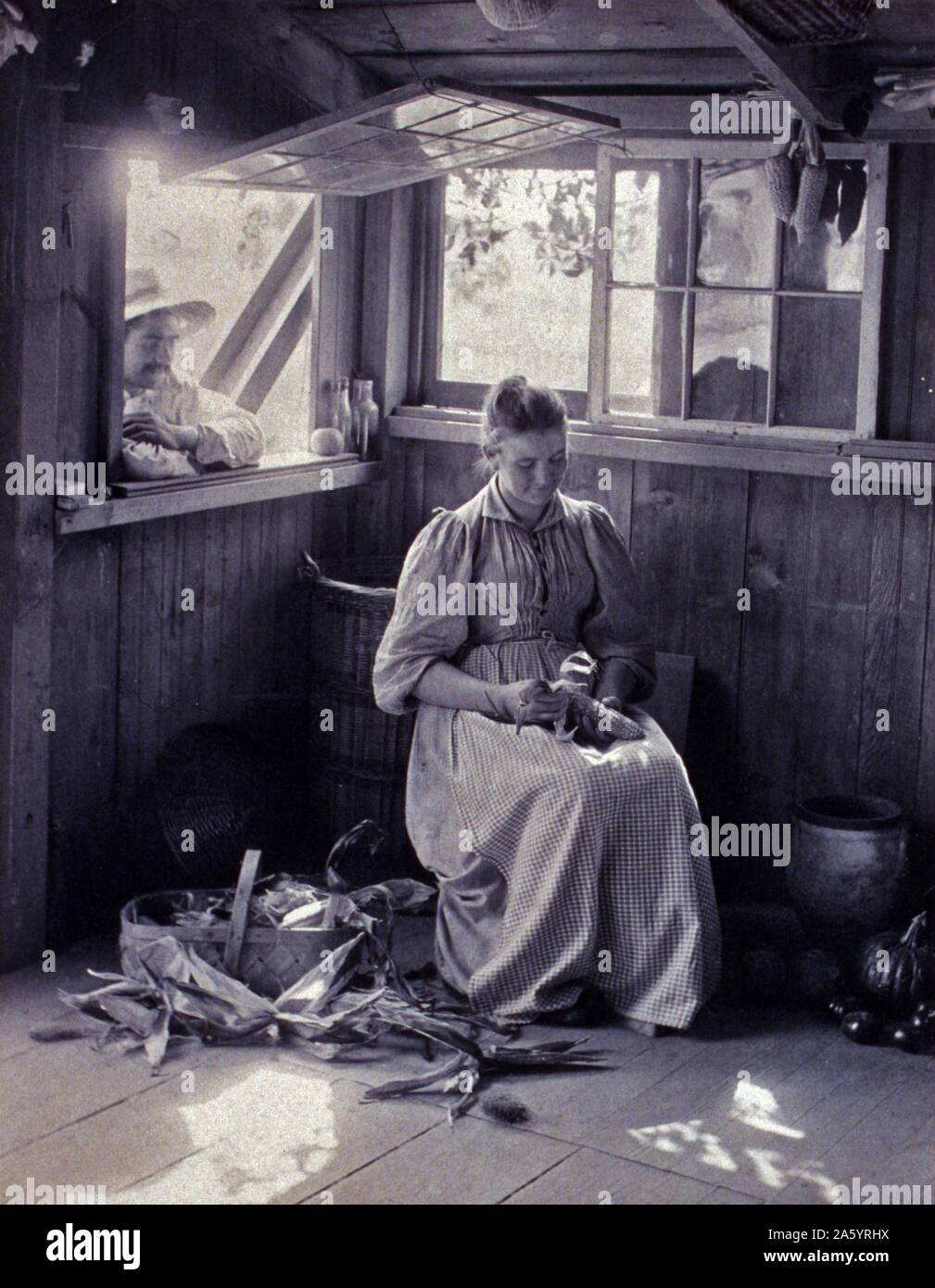 La fotografia mostra la scena rustico di una donna seduta shucking corn mentre un uomo al di fuori si appoggia sul davanzale della finestra. da Sarah Jane Eddy, 1851-1945, fotografo Foto Stock