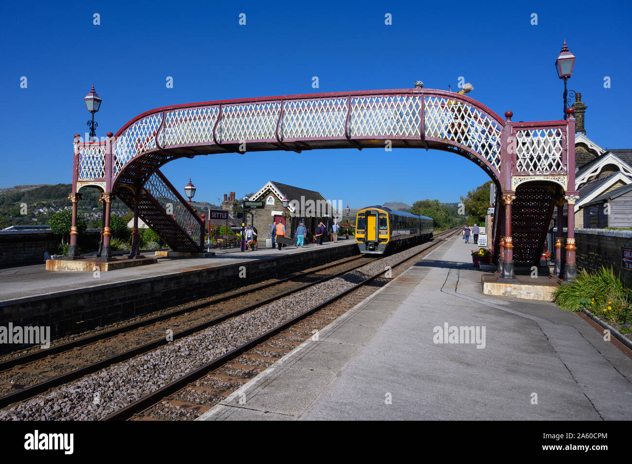 Un treno si siede presso la piattaforma a Settle stazione ferroviaria, North Yorkshire, sulla famosa arrivino a Carlisle linea con Pen-y-Ghent cadde in distanza. Foto Stock