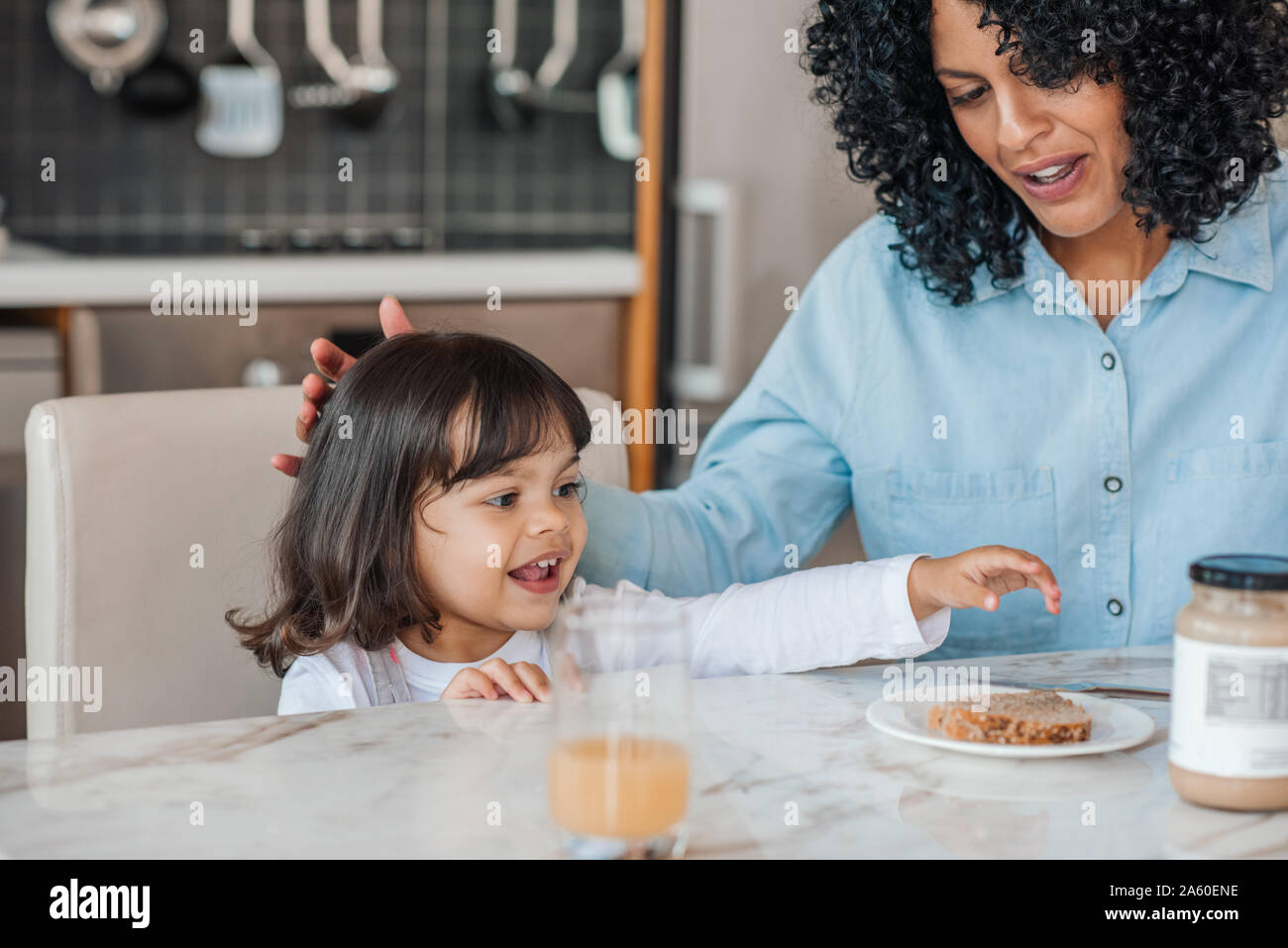 Sorridente bambina avente la prima colazione con la sua mamma a casa Foto Stock