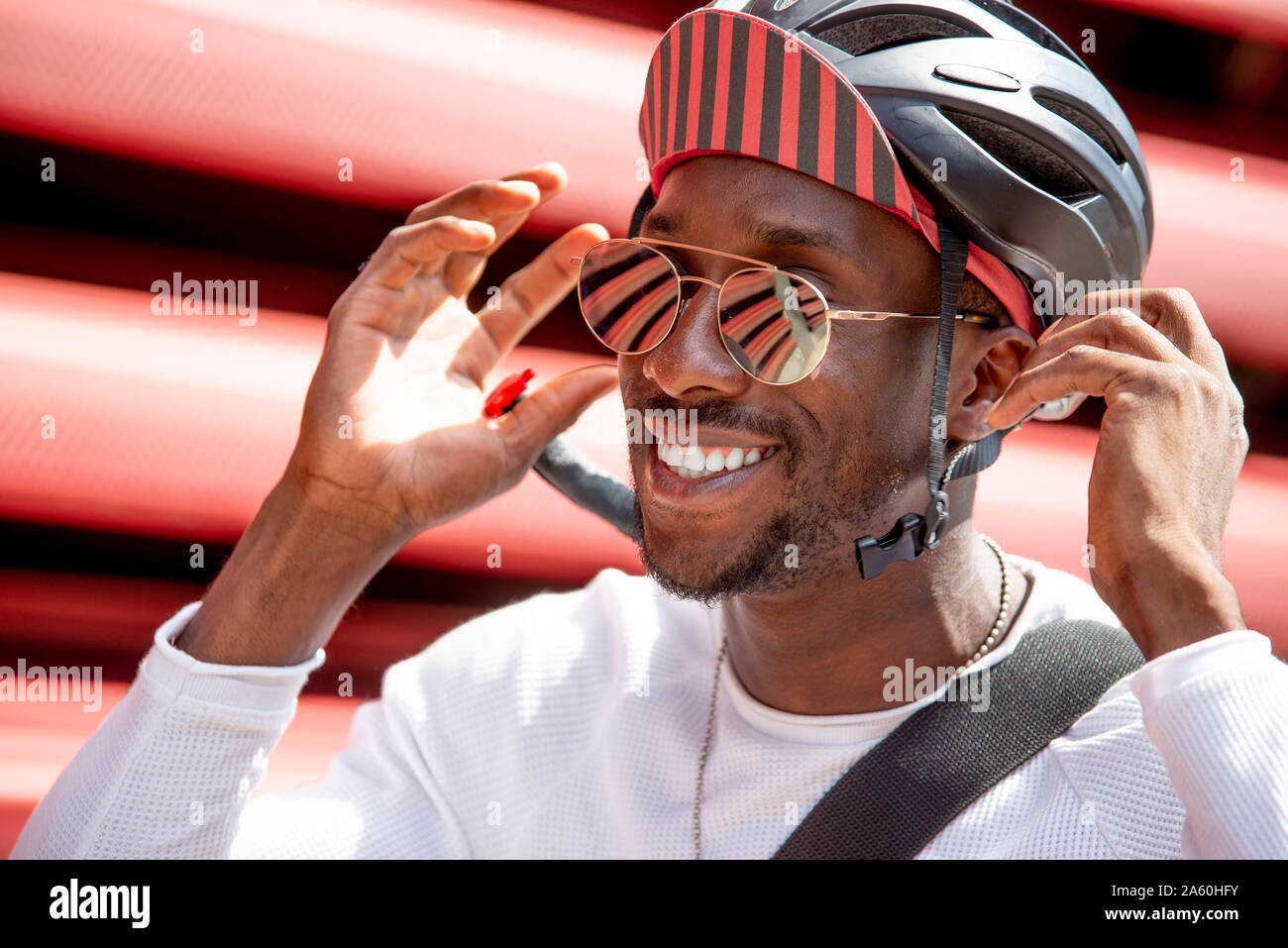 Sorridente giovane mettendo sul suo casco ciclismo Foto Stock