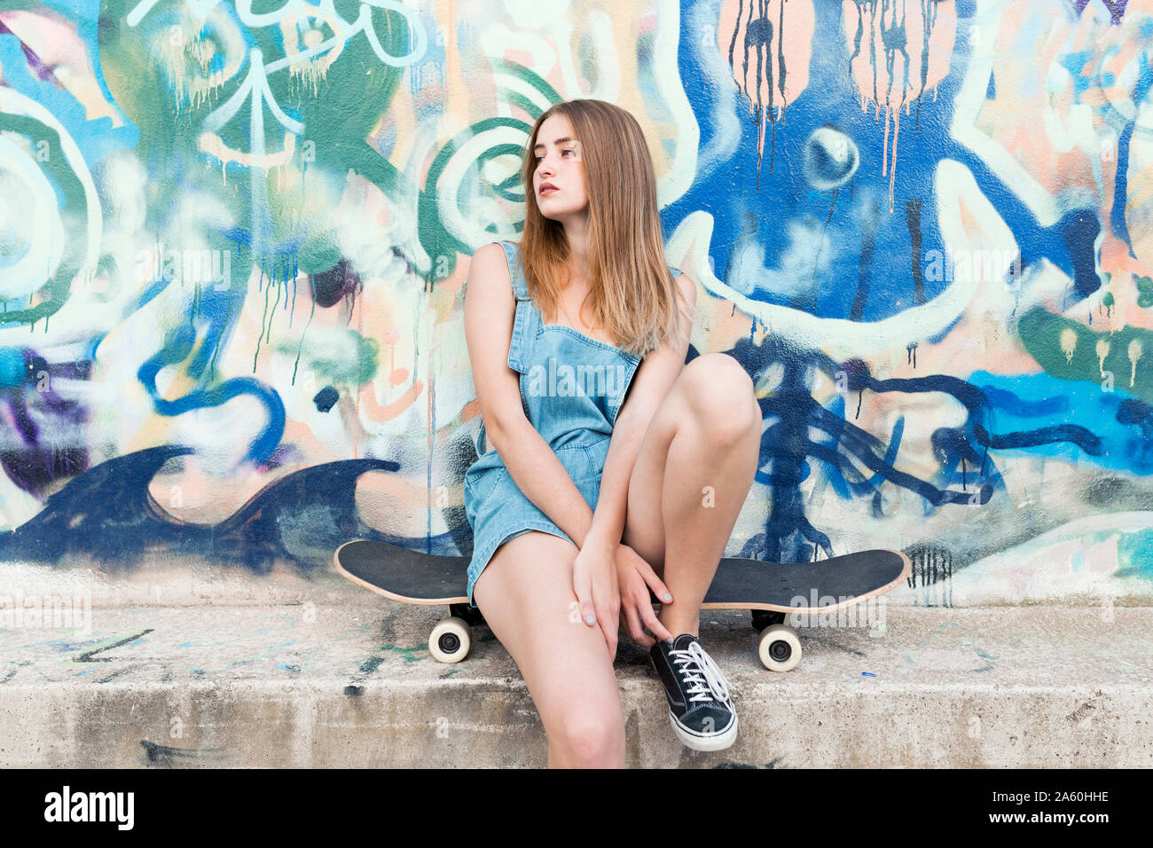 Giovane donna seduta su skateboard in parte anteriore del graffiti Foto Stock