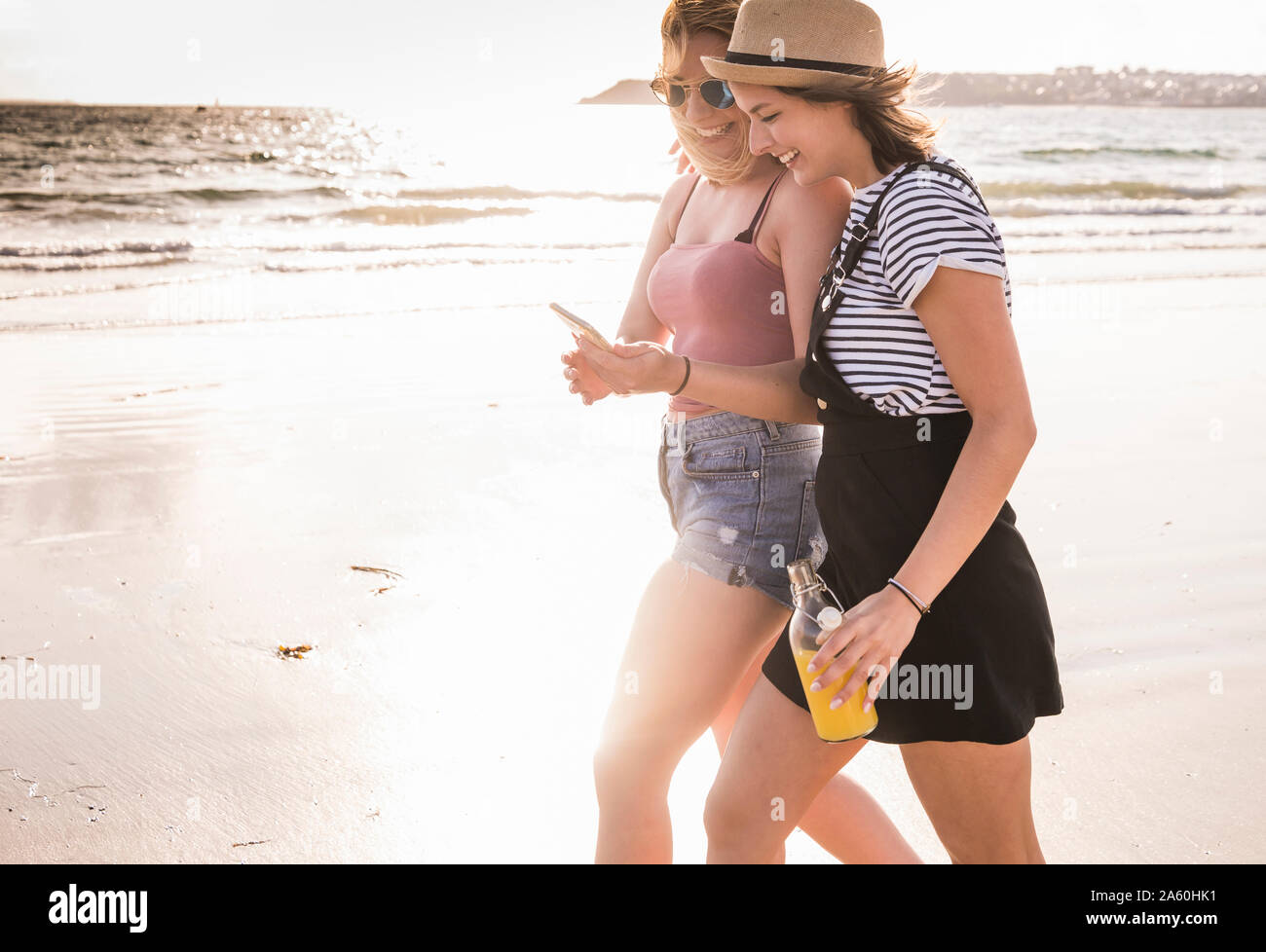 Due amiche divertendosi, passeggiate sulla spiaggia, tenendo selfies dello smartphone Foto Stock
