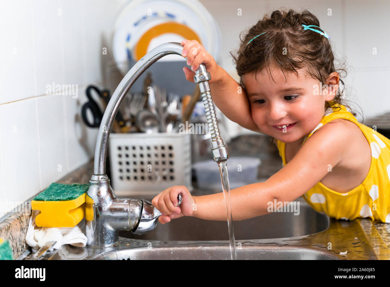 Bambina gioca con acqua del rubinetto da cucina a casa Foto Stock