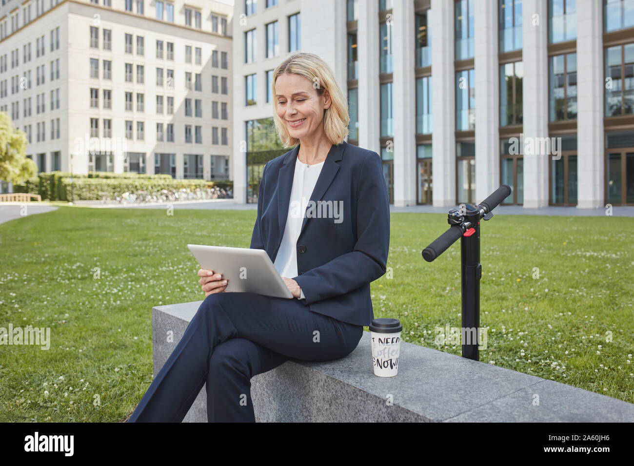 Imprenditrice seduta su di una parete della città utilizzando tablet Foto Stock