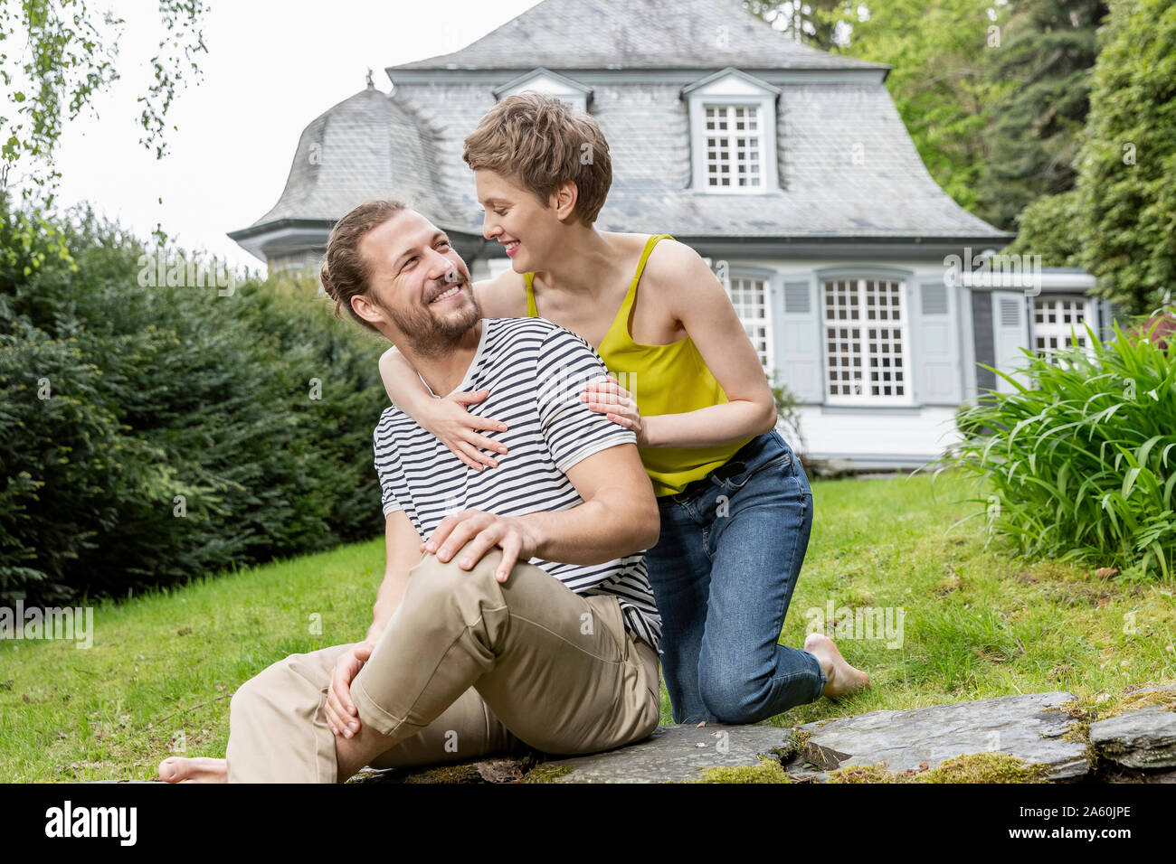 Donna felice abbracciando uomo su una parete nel giardino della loro casa Foto Stock