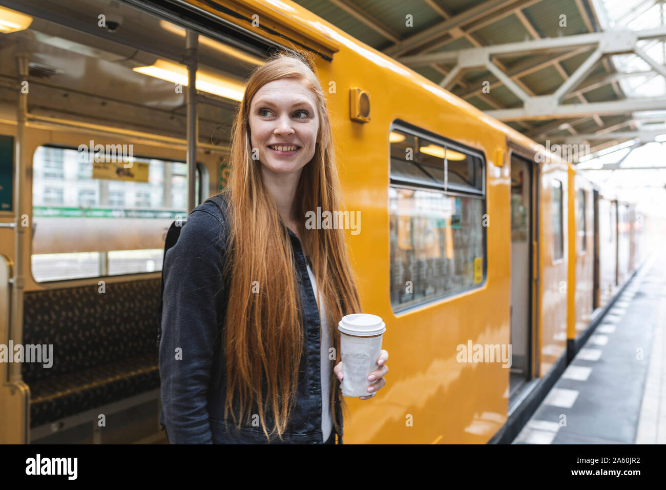 Ritratto di redheaded giovane donna con il caffè per andare uscendo dalla stazione, Berlino, Germania Foto Stock