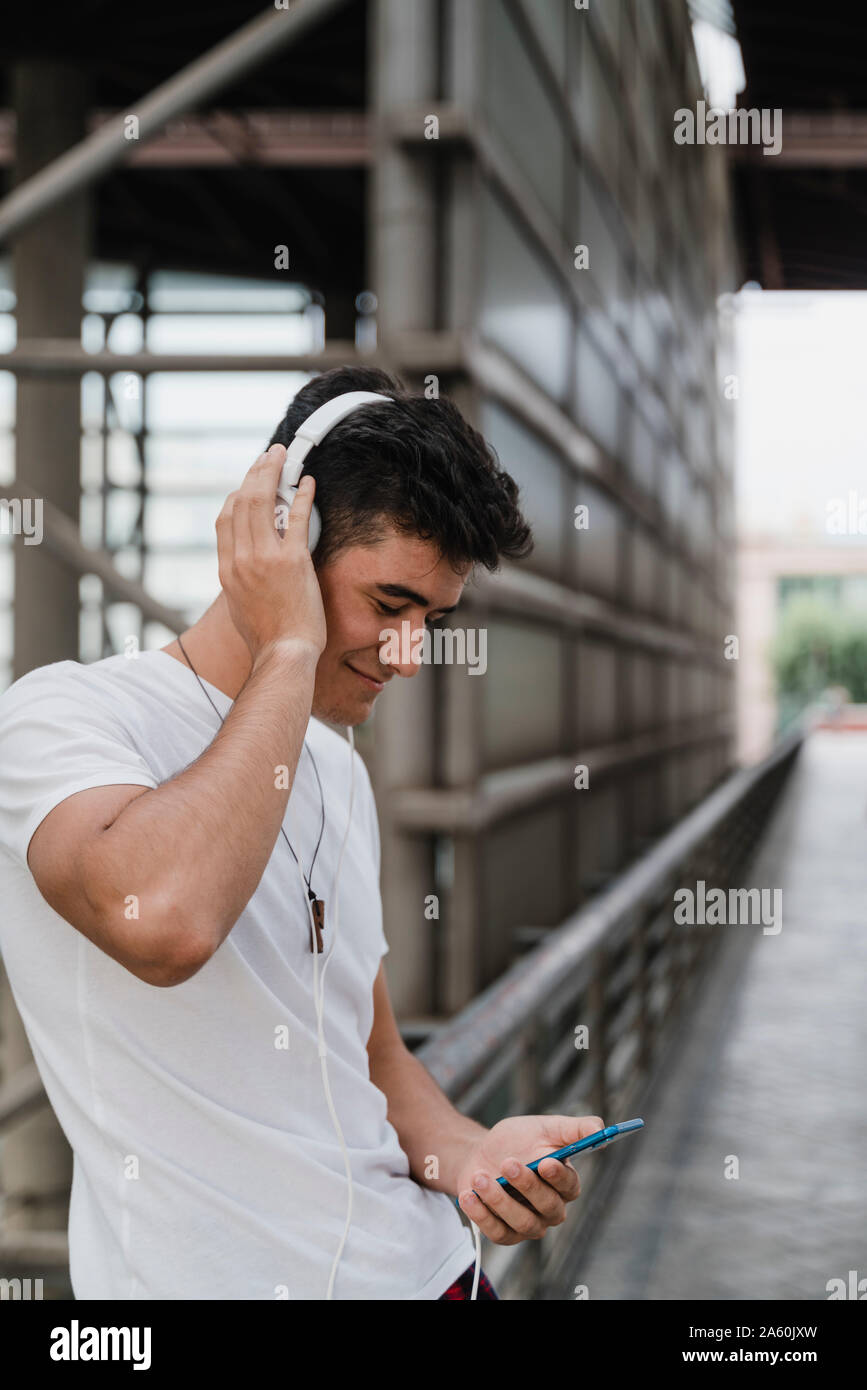 Giovane uomo in attesa alla stazione ferroviaria con lo smartphone e di indossare le cuffie Foto Stock